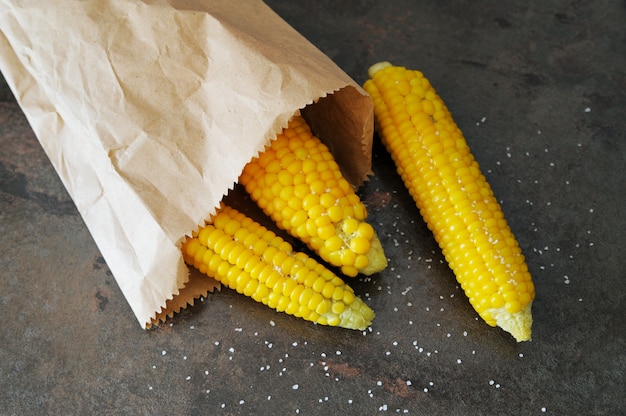 Sweet corn on the cob is in a paper bag on the table with salt.