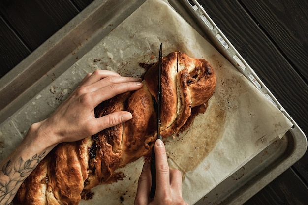 Photo sweet cottage cheese braided bread with raisins and jam. slicing with a knife, female hands. overhead close-up shot.