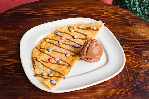 Sweet crepe with chocolate cream and ice cream on wooden background