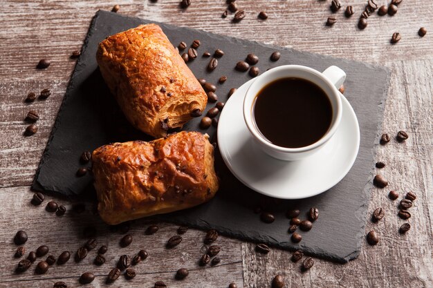 Sweet Croissants with almonds, hot coffee and spreaded coffee beans. Sweet breakfast