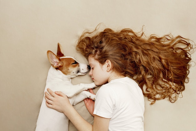 甘い巻き毛の少女とジャックラッセル犬は夜寝ています。