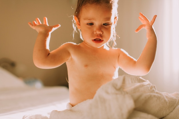 Photo sweet curly little girl with a towel over her wet body siting in a bedroom after shower