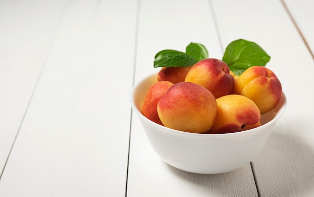 Сладкий вкусный абрикос на темной миске белого дерева стол летом свежие фрукты