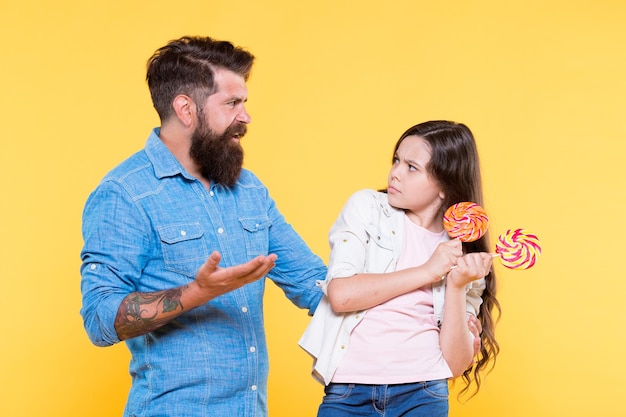 Dessert dolce hipster barbuto buon papà per una figlia adorabile condividere dolci con le persone più care figlia e padre mangiano caramelle dolci infanzia dolce bambina e papà tengono lecca-lecca colorati