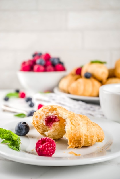 Dessert dolce, mini croissant al forno fatti in casa con marmellata di bacche, servito con tè, lamponi freschi, mirtilli e menta