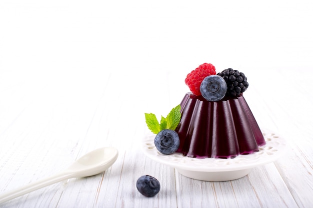 Sweet dessert jelly pudding with berries raspberries blackberries blueberries on white plate