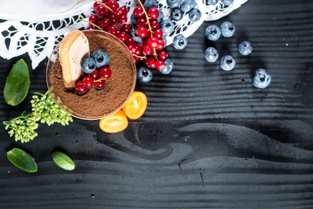 Sweet dessert tiramisu with blueberries and currants on black