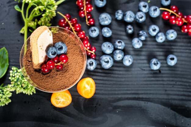 Sweet dessert tiramisu with blueberries and currants on black