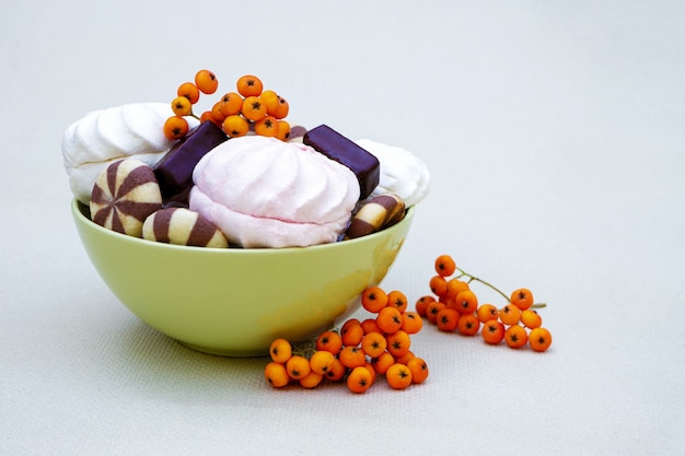 Sweet dessert of white and pink marshmallows with cookies and chocolates with rowan fruits.