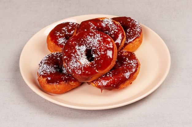 Sweet donuts in caramel glaze in a pink plate on a gray  close up