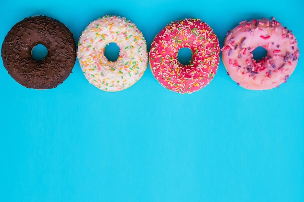 sweet donuts of different colors are arranged in a row on a blue background.