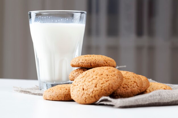 Not sweet but dry and crunchy cookies with added sugar, hard cookies baked with oatmeal and wheat flour, low-calorie oatmeal cookies on the table, a glass of white fresh milk