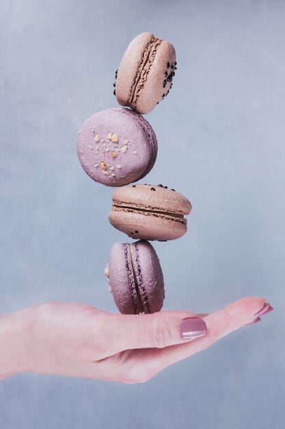 Sweet french macarons cookies stacked on woman's hand against grey surface. Pastel colored flying macaroons. Food, culinary and cooking concept