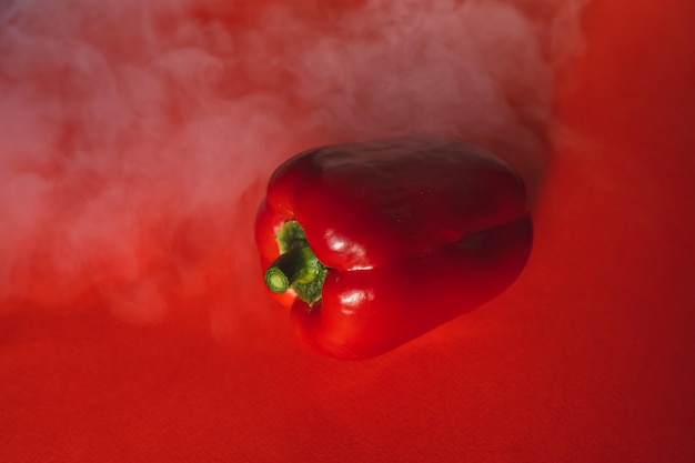 Sweet fresh red pepper on a red background with a light smoke