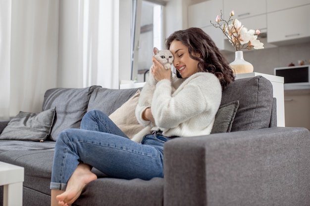 Sweet friend. Young woman in white sweater and her cat at home