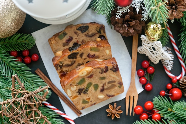 Photo sweet fruit cake slices on white paper put on black granite table in top view flat lay with christmas decoration