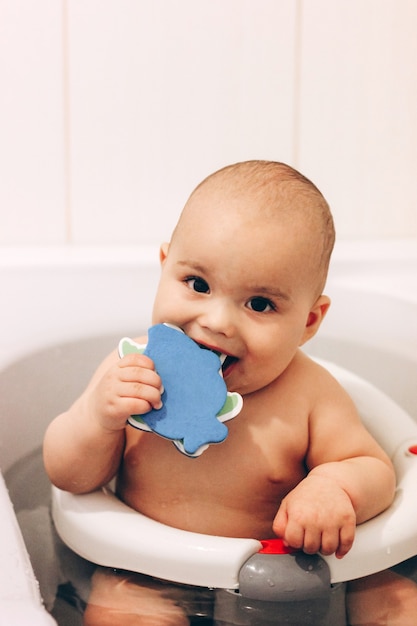 Bambino dolce e divertente che fa il bagno. bambino che mastica un giocattolo su una sedia da bagno. balneazione di sicurezza.