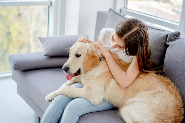 Sweet girl holding cute dog sitting on sofa indoors