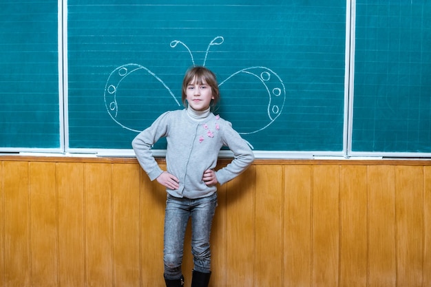 Sweet girl is standing by the school board where the chalk drawn butterfly