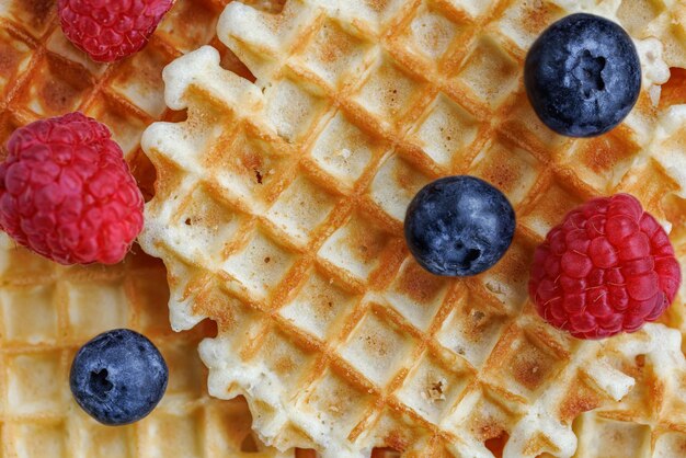 Sweet golden Belgian waffles with fresh raspberries and blueberries. Delicious breakfast.