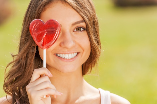 Sweet happiness. Young beautiful women holding lollipop in front of her eye and smiling while standing outdoors