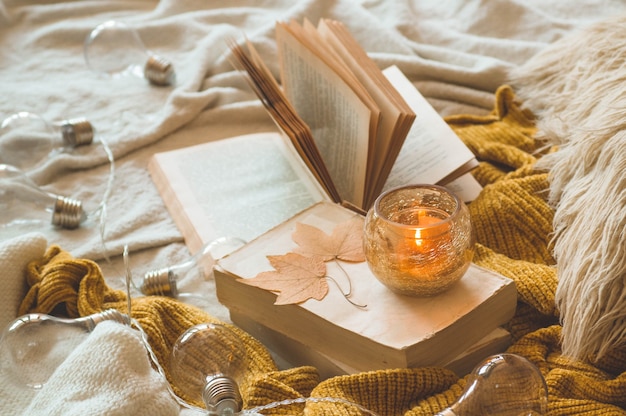 Sweet Home. Still life details in home interior of living room. Sweaters and candle,  autumn decor on the books. Read, Rest. Cozy autumn or winter concept.