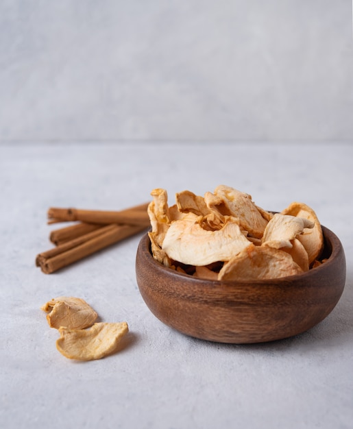 Сладкие домашние яблочные чипсы запеченные с корицей в деревянной миске на сером фоне. Веганский и диетический продукт
