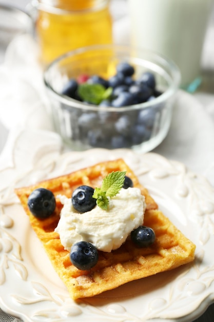 Sweet homemade waffles on plate on color wooden background