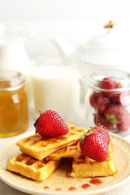 Sweet homemade waffles with fresh strawberries on plate, on light background