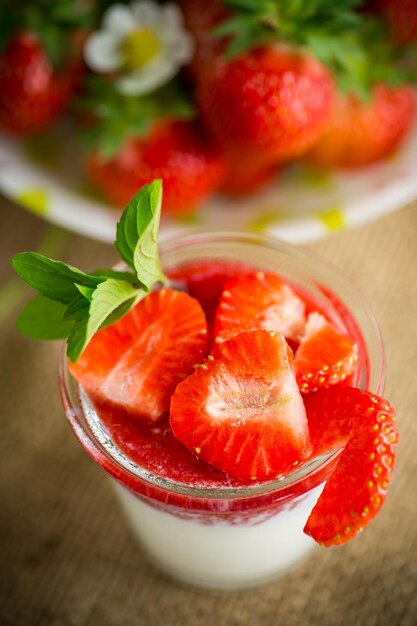 Sweet homemade yogurt with strawberry jam and fresh strawberries in a glass cup