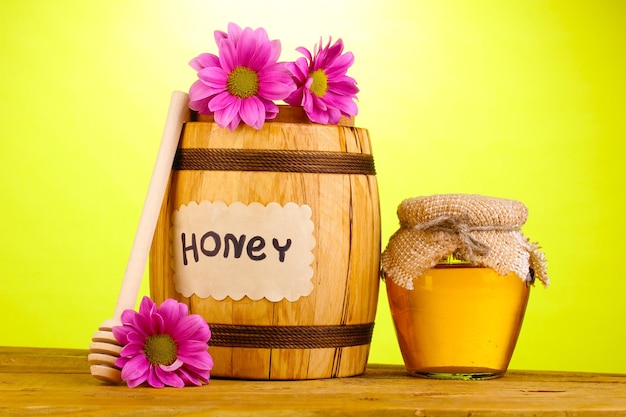 Sweet honey in barrel and jar with drizzler on wooden table on green background