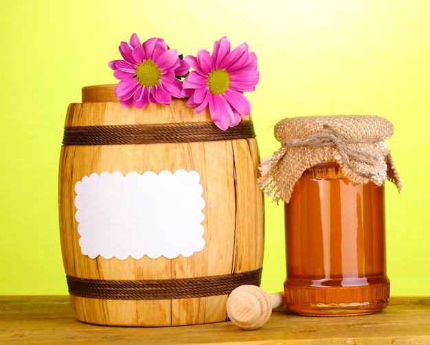 Sweet honey in jar and barrel with drizzler on wooden table on green background