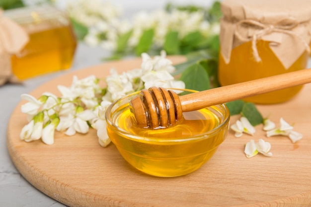 Sweet honey jar surrounded spring acacia blossoms Honey flows from a spoon in a jar jars of clear fresh acacia honey on wooden background