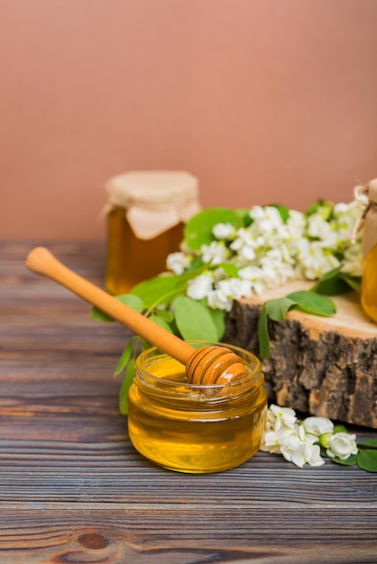 Sweet honey jar surrounded spring acacia blossoms honey flows\
from a spoon in a jar jars of clear fresh acacia honey on wooden\
background