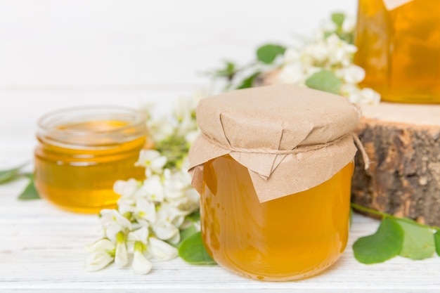 Sweet honey jar surrounded spring acacia blossoms Honey flows from a spoon in a jar jars of clear fresh acacia honey on wooden background