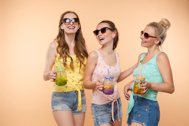 Sweet Life Three beautiful slender women in summer clothes with cocktails are laughing having a good time together Studio isolated background The concept of recreation