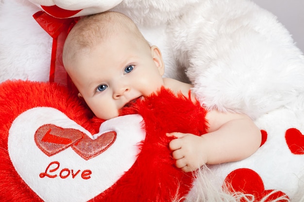 Photo sweet little baby hugs the heart in the paws of a large plush bear