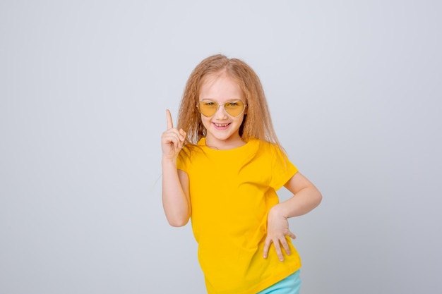 Photo a sweet little cheerful happy girl in sunglasses is happy lying on a white background showing dif