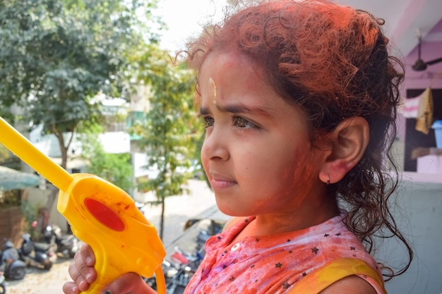 Sweet little indian girl playing colours on holi festival holding pichakaree full of colours holi festival celebrations in delhi india