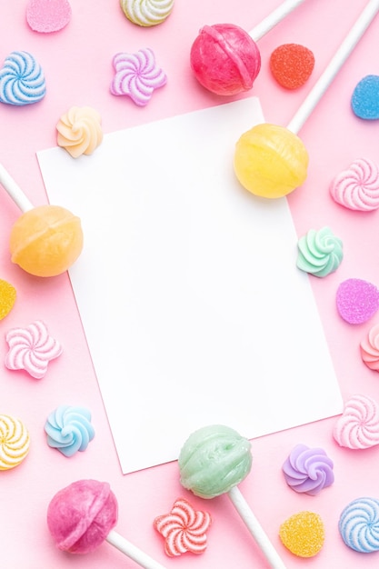 Photo sweet lollipops and candies and blank greeting card on pink background