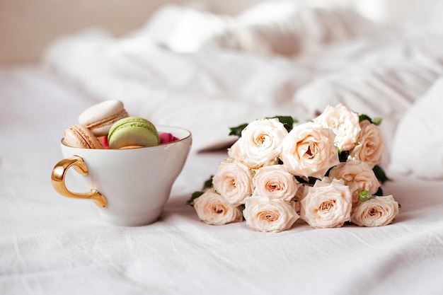 Sweet macaroons in mug and white roses