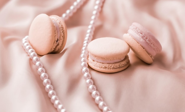 Sweet macaroons and pearls jewellery on silk background parisian chic jewelry French dessert food and cake macaron for luxury confectionery brand holiday gift