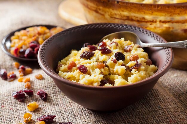 Sweet millet porridge with raisins and dried cranberries in ceramic rustic bowl