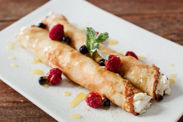 Sweet pancake with cottage cheese close up. Homemade rolled dessert with raspberries on white plate.