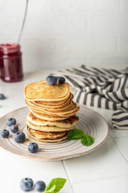 Sweet pancakes for breakfast in a stack on a ceramic plate with fresh blueberries and mint light key...