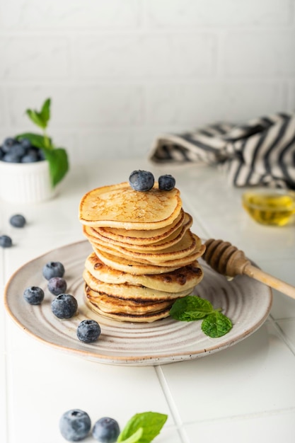 Sweet pancakes for breakfast in a stack on a ceramic plate with fresh blueberries and mint light key...