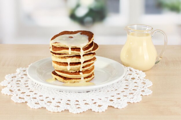 Sweet pancakes on plate with condensed milk on table in kitchen