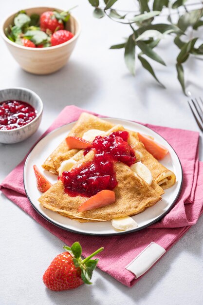 Sweet pancakes with berry jam fresh strawberries and banana on a light background The concept of homemade food