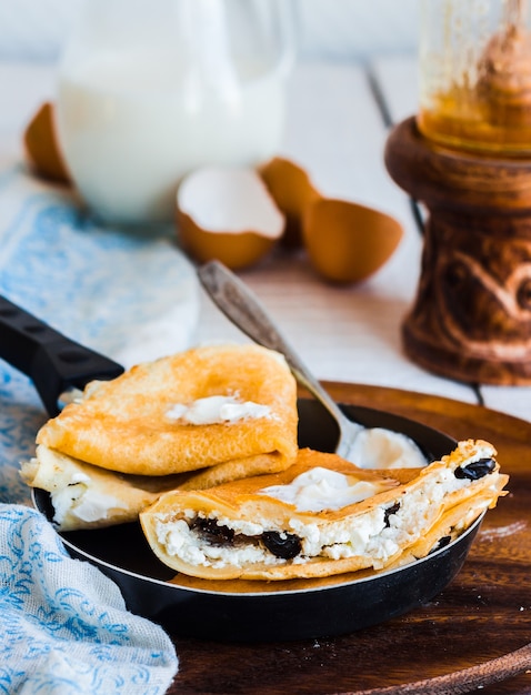 Sweet pancakes with cottage cheese, prunes, honey and sour cream, rustic, in a frying pan