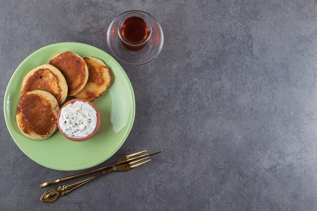 Sweet pancakes with sour cream and glass of tea on table.